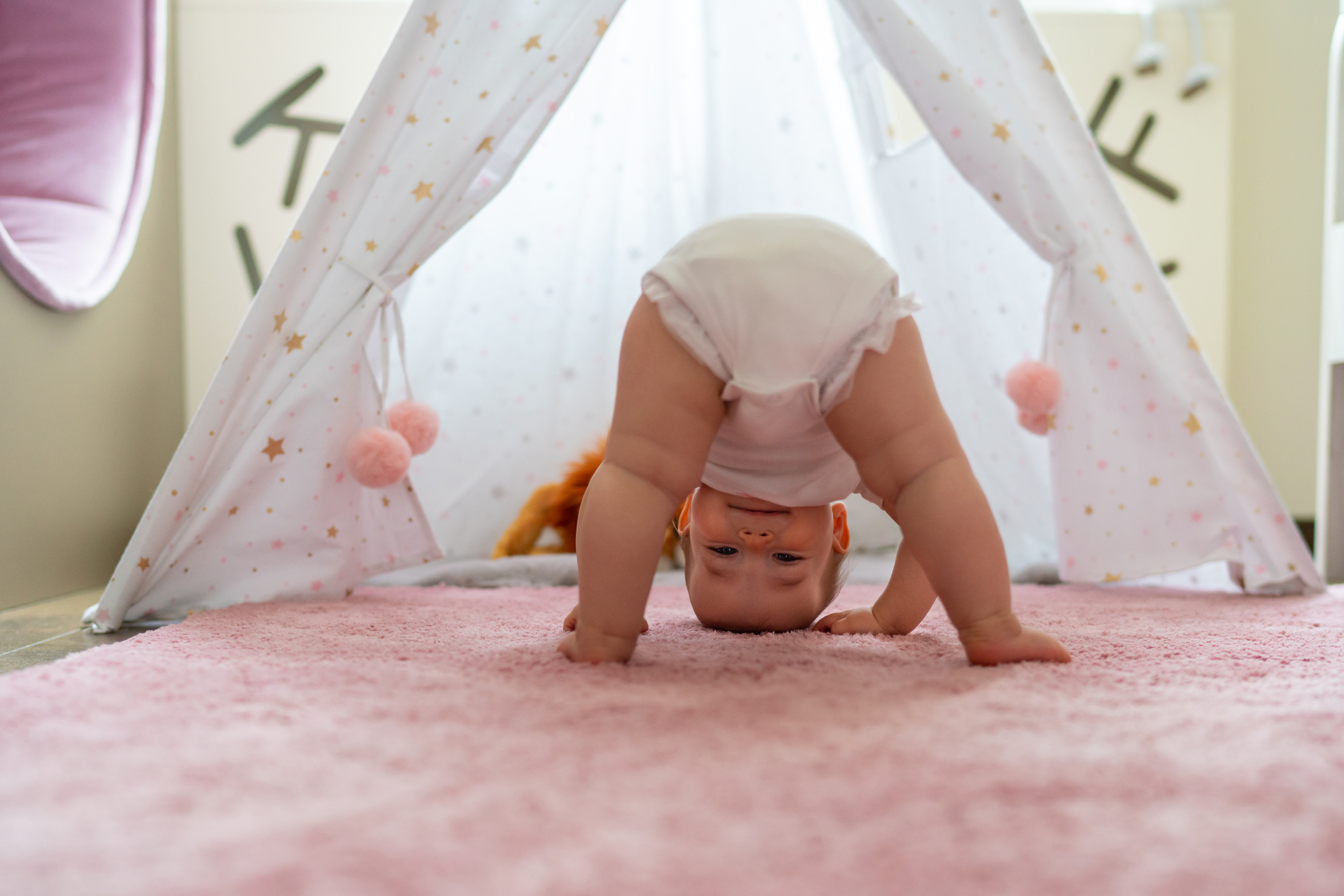 Baby standing with their head on a pink rig looking back between their legs