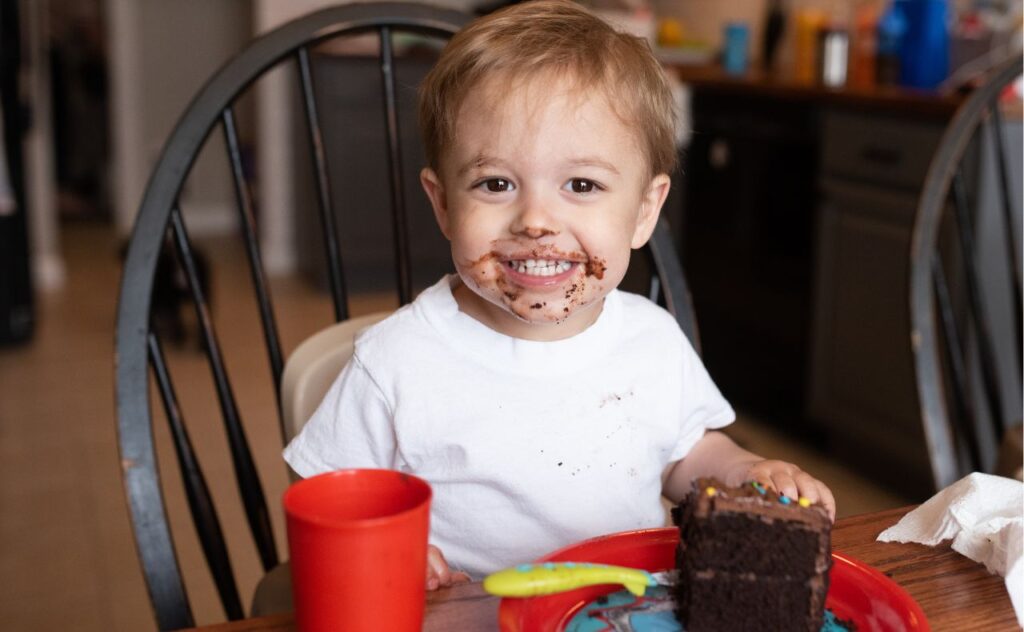 Too much sugar? Toddler with chocolate on face, eating cake.