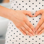 Closeup on young woman holding hands in heart shape on her belly
