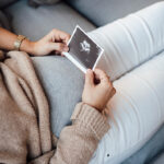 Pregnant woman holding ultrasound photo at home