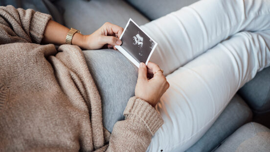 Pregnant woman holding ultrasound photo at home