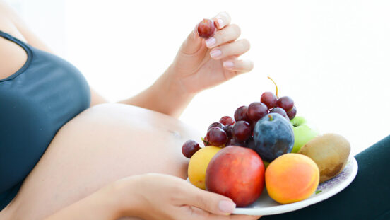 Pregnant woman holding fruits on a plate in front of her belly