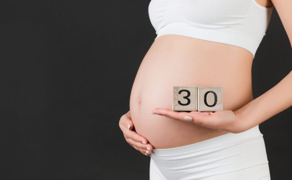 Pregnant woman holding wooden block- that say 30 for 30 weeks pregnant