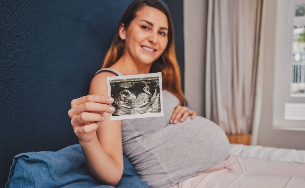 Pregnant woman 28 weeks holding up sonogram scan