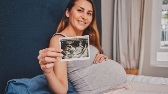 Pregnant woman 28 weeks holding up sonogram scan