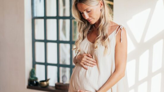 Beautiful pregnant woman touching her belly standing by the window