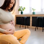 Young happy pregnant woman is sitting on the floor in the living room