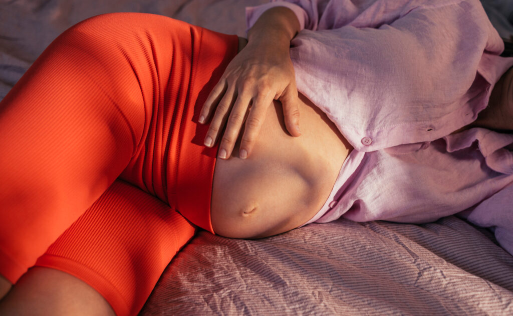 A from above view of an anonymous Caucasian future mother holding her stomach while lying on the bed.