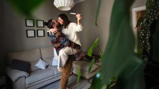 A man holds his partner in his arms to celebrate his positive pregnancy test at home