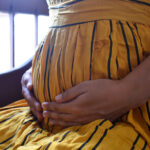 Six months pregnant woman sitting and touching belly near the window closeup