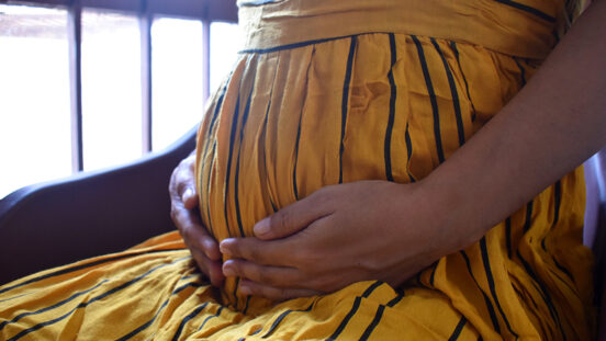 Six months pregnant woman sitting and touching belly near the window closeup