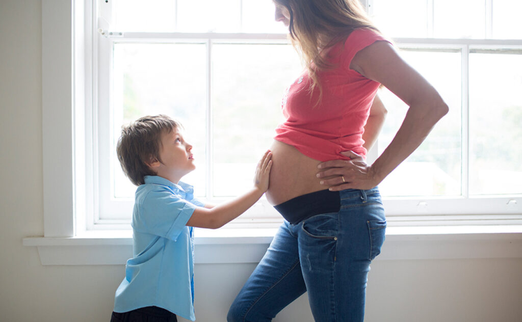 UYpung boy rubs mums heavily pregnant belly in front of light filled window