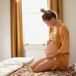Heavily pregnant woman sitting on bed holding stomach