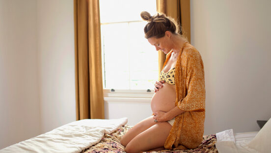 Heavily pregnant woman sitting on bed holding stomach