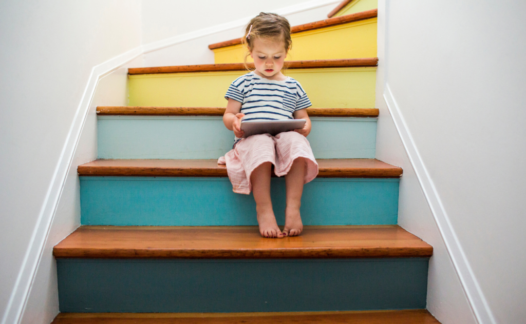 little girl reading a book sitting on a colourful staircase