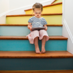 little girl reading a book sitting on a colourful staircase