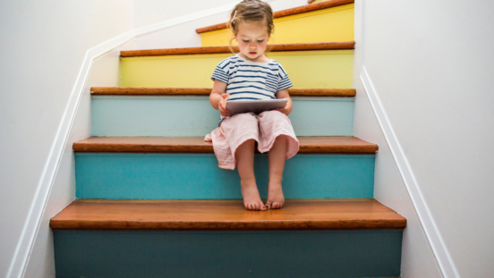 little girl reading a book sitting on a colourful staircase