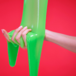 Hand held out against red background as green slime is poured onto it.