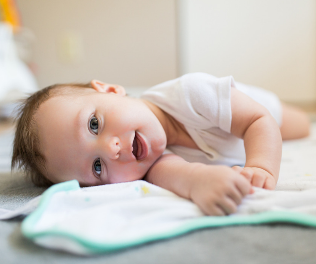 Smiling baby laying a on a bed in a sun filled room.