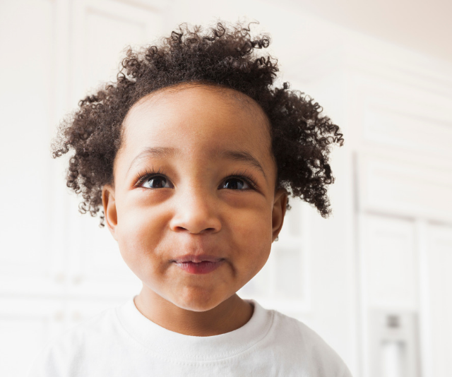 Cute curly haired toddler with cheeky grin, sitting in a sun filled room.