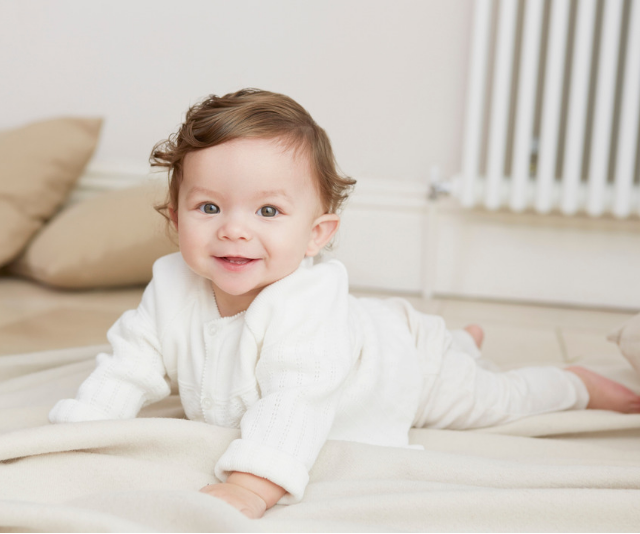 Cute curly haired baby doing tummy time on a floor rug.