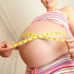 Pregnant woman measuring the size of baby bump with tape measure