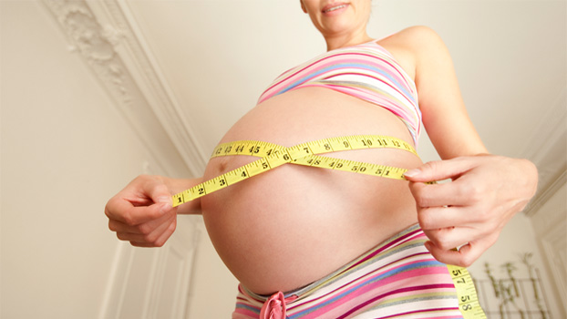 Pregnant woman measuring the size of baby bump with tape measure