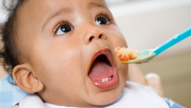 Infant with dark hair, mouth wide open to take a spoonful of food