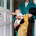 Tired mum in gown carrying baby and laundry