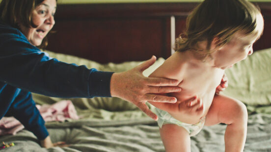 A senior woman playing with her young granddaughter on her bed in her bedroom.