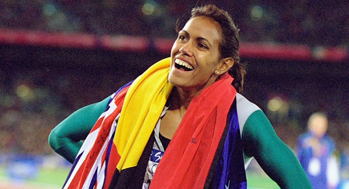 Smiling Cathy Freeman at the 2000 Olympics weraing the Australin and Aboriginal flags around her shoulders