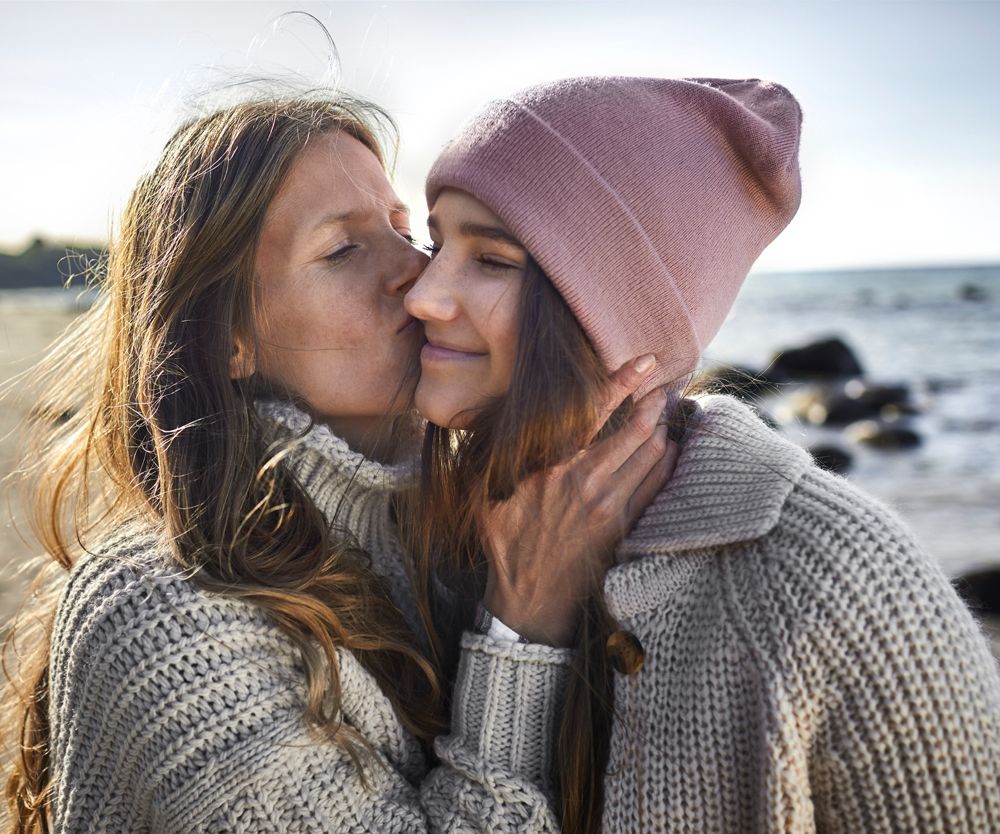 Mother kisses teenage daughters cheek.