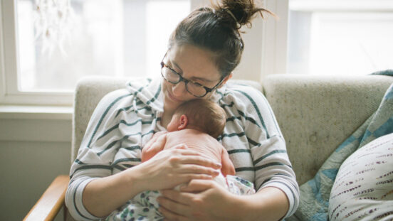 A mother holds her newborn baby boy close to her chest while seated and resting on a white sofa.