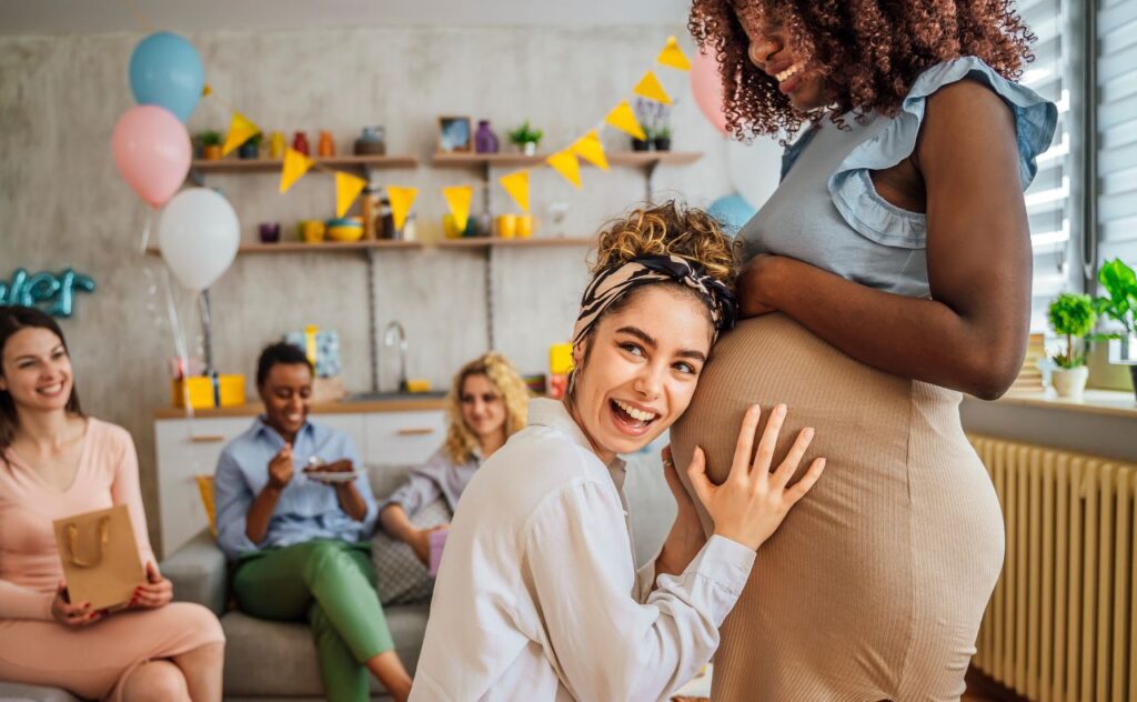 Active baby: Woman at a baby shower with her ear pressed against her friend's pregnant tummy 