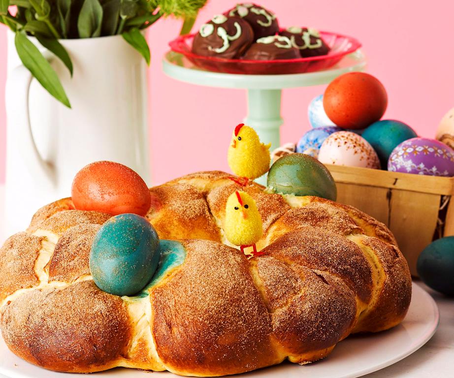 Round loaf of Easter bread decorated in colourful dyed eggs and tiny chick decorations