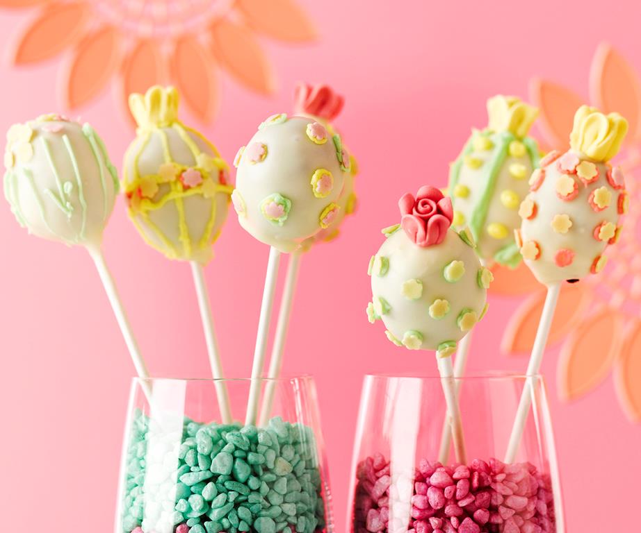 Two glasses filled with small colourful beads and decorated yellow cake pops standing up like flowers