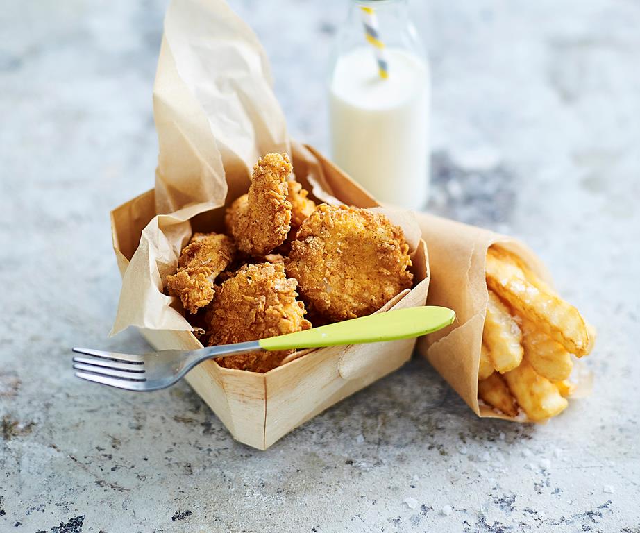 Small container of chicken nuggets next to a glass of milk