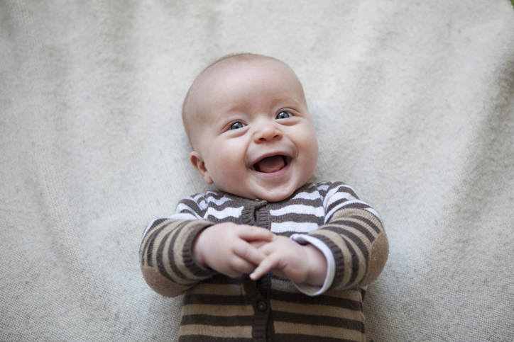 Laughing baby wearing a striped sweater and holding their hands together