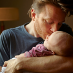 Red headed, bearded dad holding his baby close and kissing him on the head