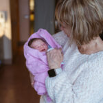 A beautiful moment that shows a grandmother in her sixties holding her newborn granddaughter for the first time in the hospital room.