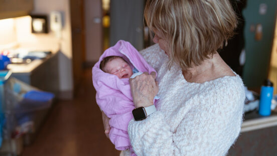 A beautiful moment that shows a grandmother in her sixties holding her newborn granddaughter for the first time in the hospital room.