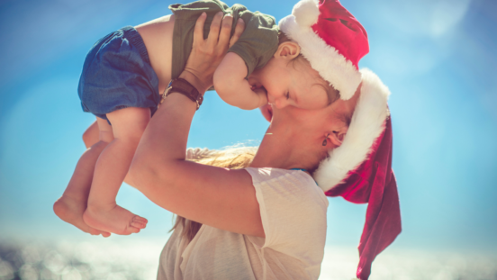 Mum wearing santa hat holding older baby boy wearing santa hat up in her arms