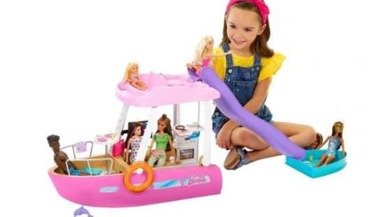 Girl in sitting on the floor playing with Barbie dolls and Barbie boat