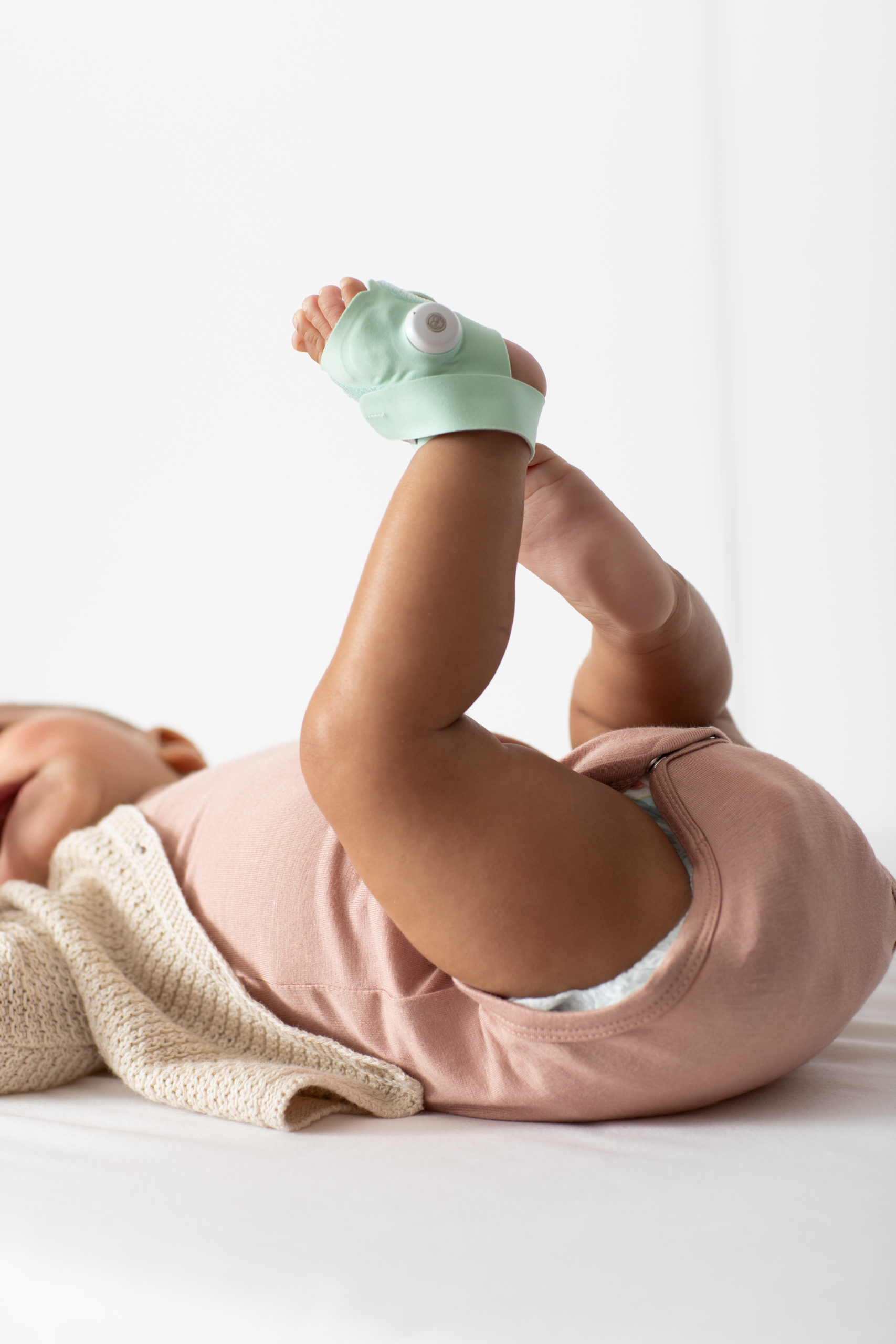 Baby lying on its back with their legs in the air, Owlet Smart Sock 3 on one foot