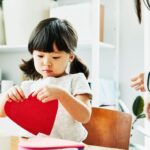 Young girl looking at paper hearts while making Valentines Day cards in home
