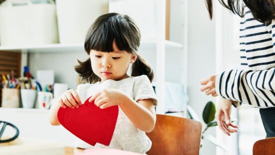 Young girl looking at paper hearts while making Valentines Day cards in home