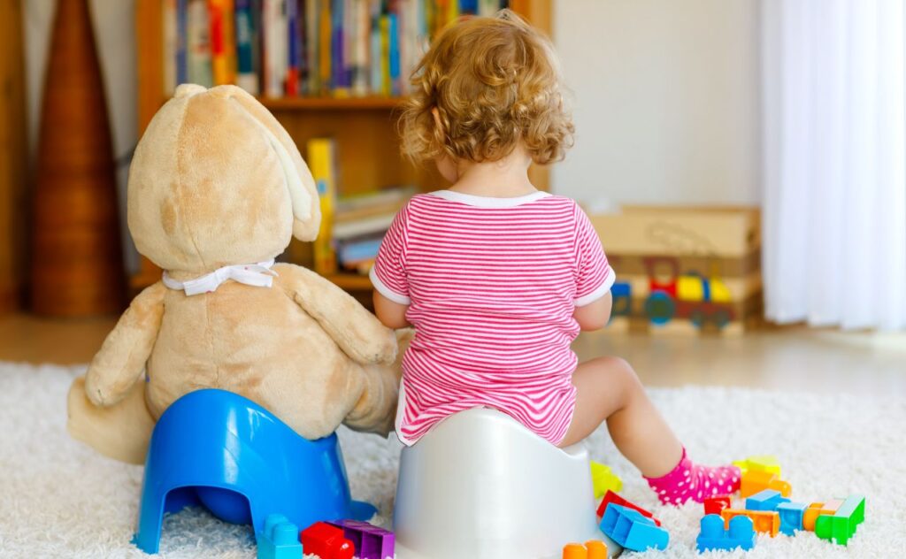 Scared of pooing: toddler baby girl child sitting on potty. Kid playing with big plush soft toy.