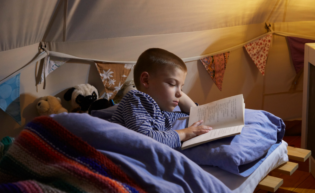 Primary school boy lying on his side reading a book in bed