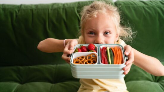 Girl on sofa showing her bento box with fruit and vegies