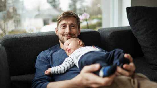 Smiling father and baby boy lying on couch.